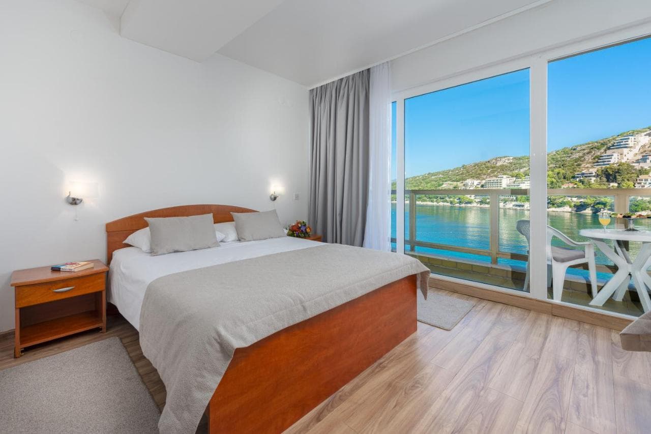 Hotel room with wooden bed and balcony overlooking the sea and green hills of Dubrovnik.