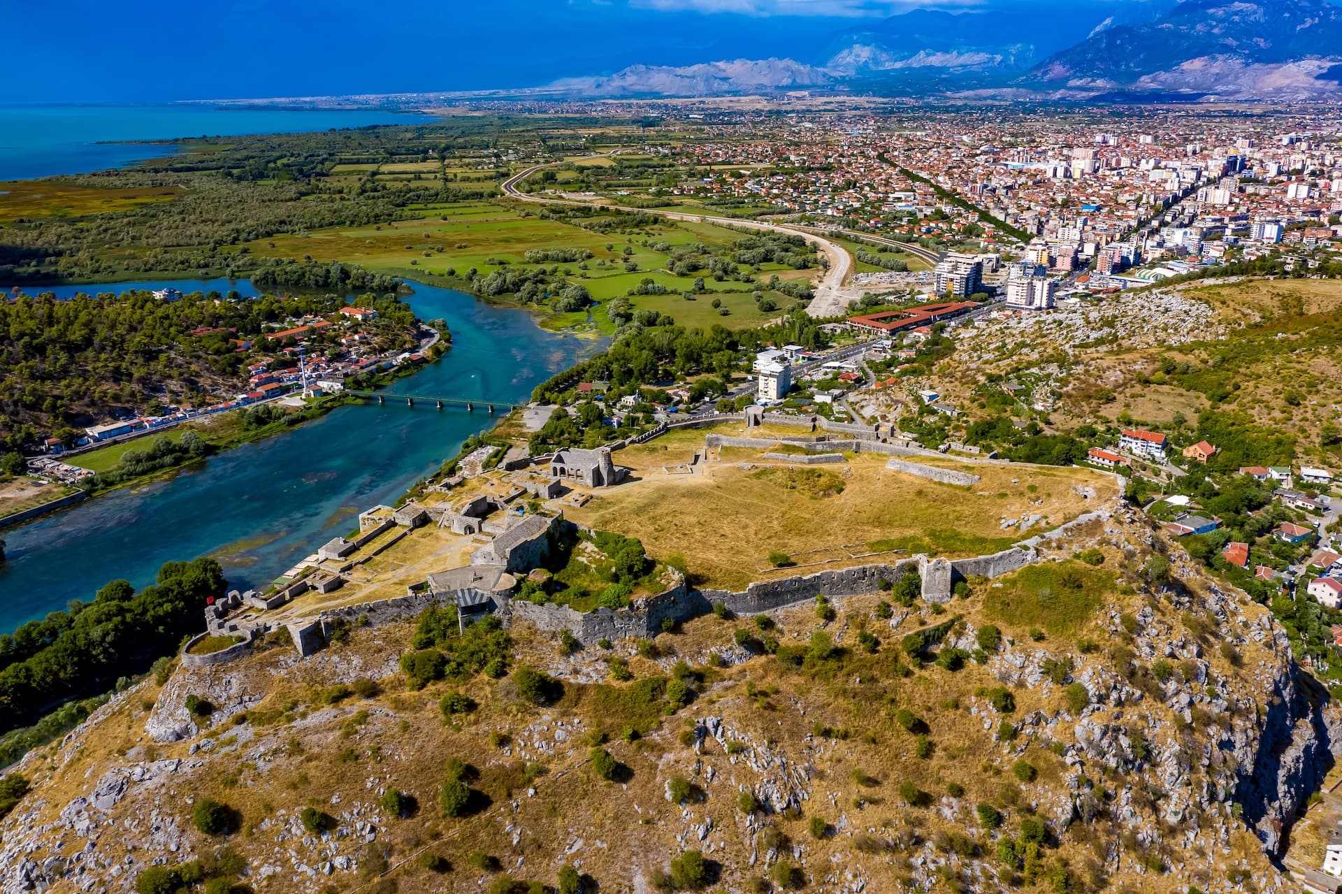 Aerial view of Rozafa Castle ruins above Shkodra, Albania, with river and city below.