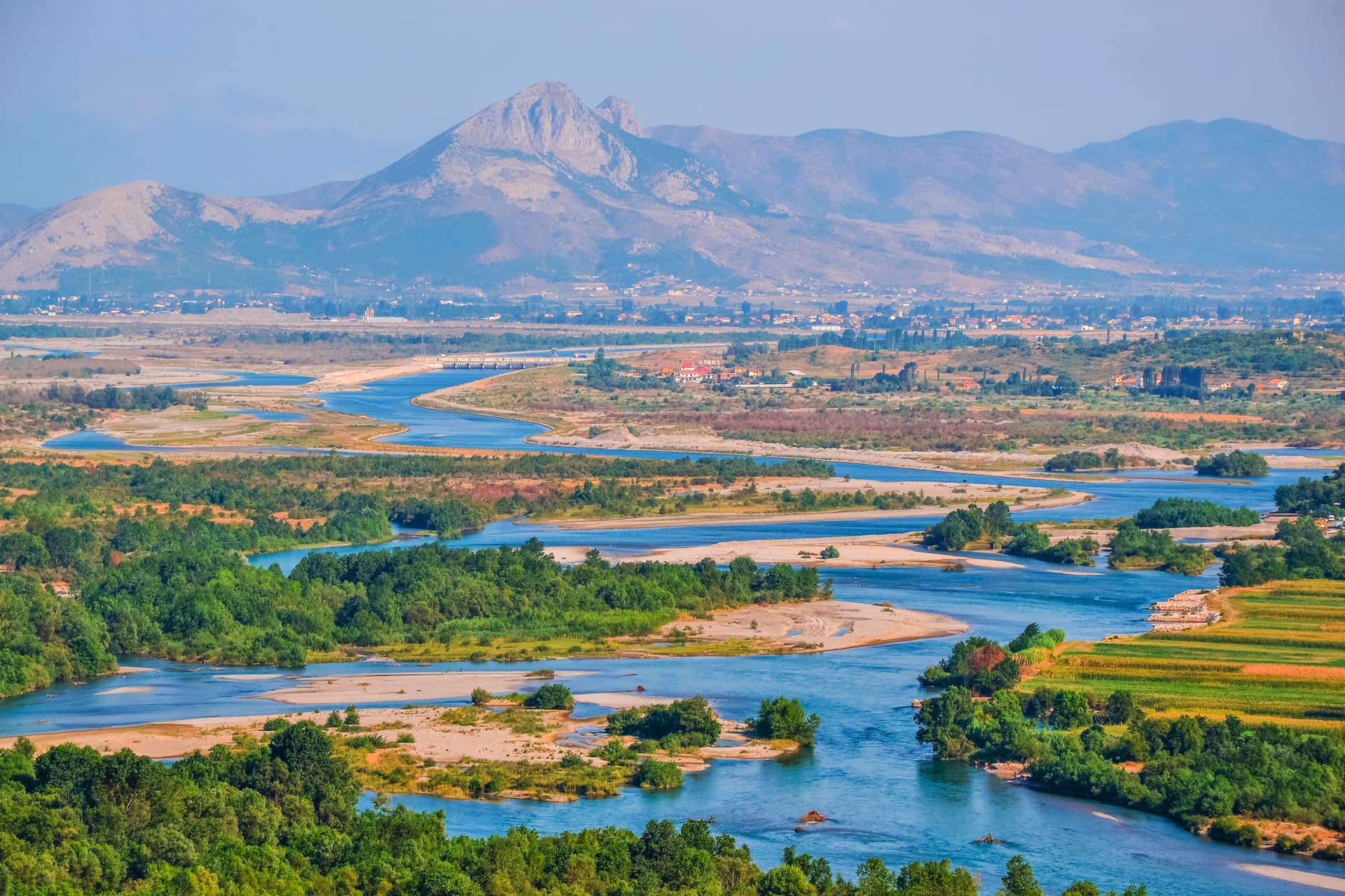 Winding Drin River with sandbars, green banks, and mountains near Shkodra, Albania.