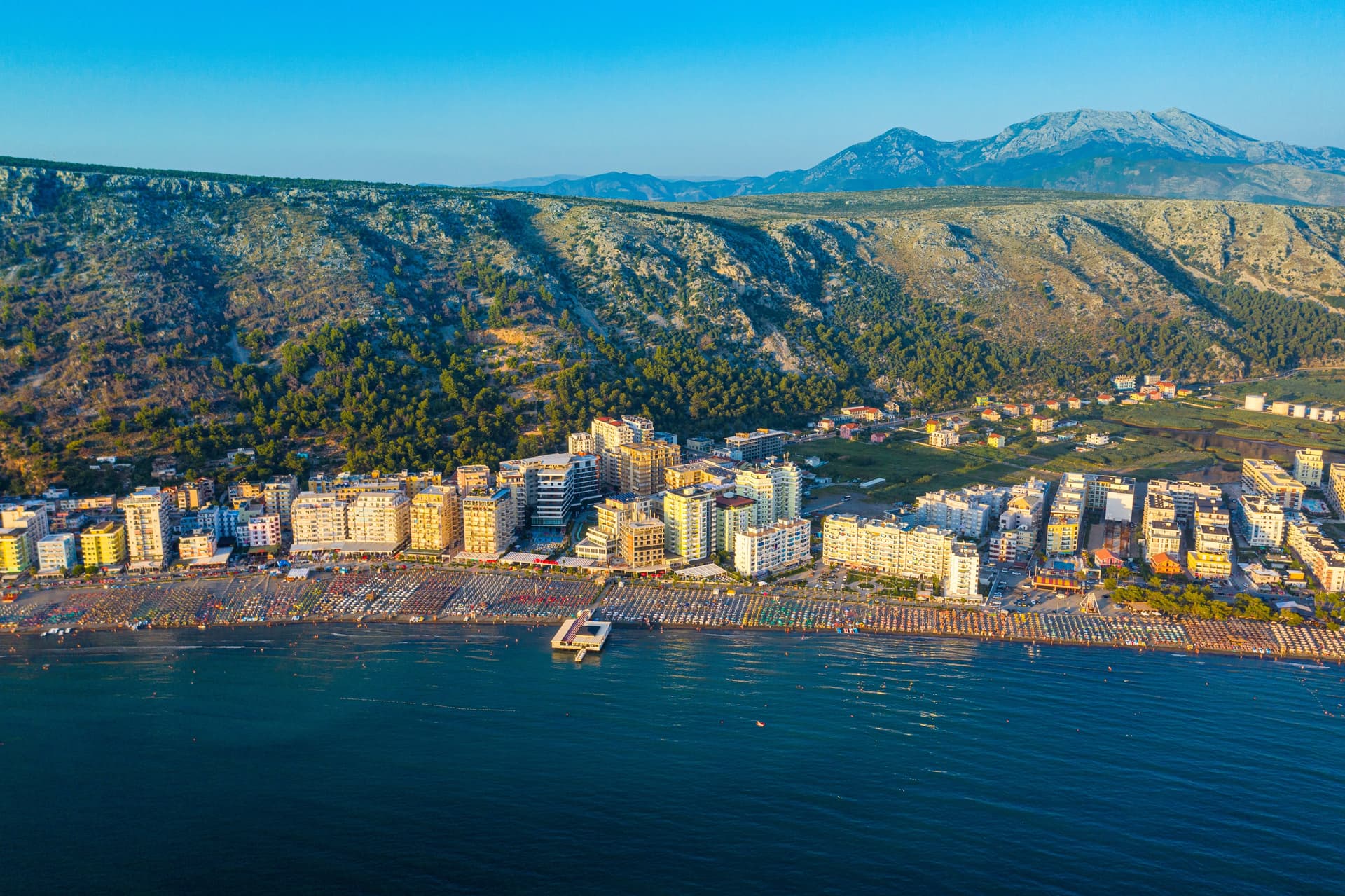 Coastal city with apartment buildings, crowded beach, and mountains in the hinterland of Albania.