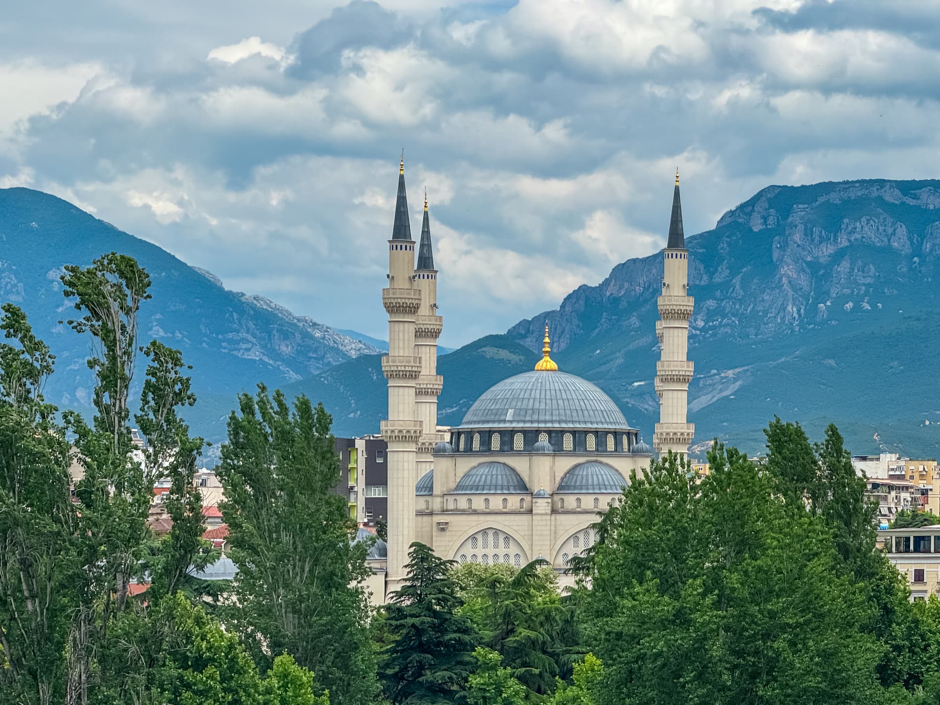Namazgah Mosque in Tirana, Albania, with minarets, dome, and mountains under cloudy sky.