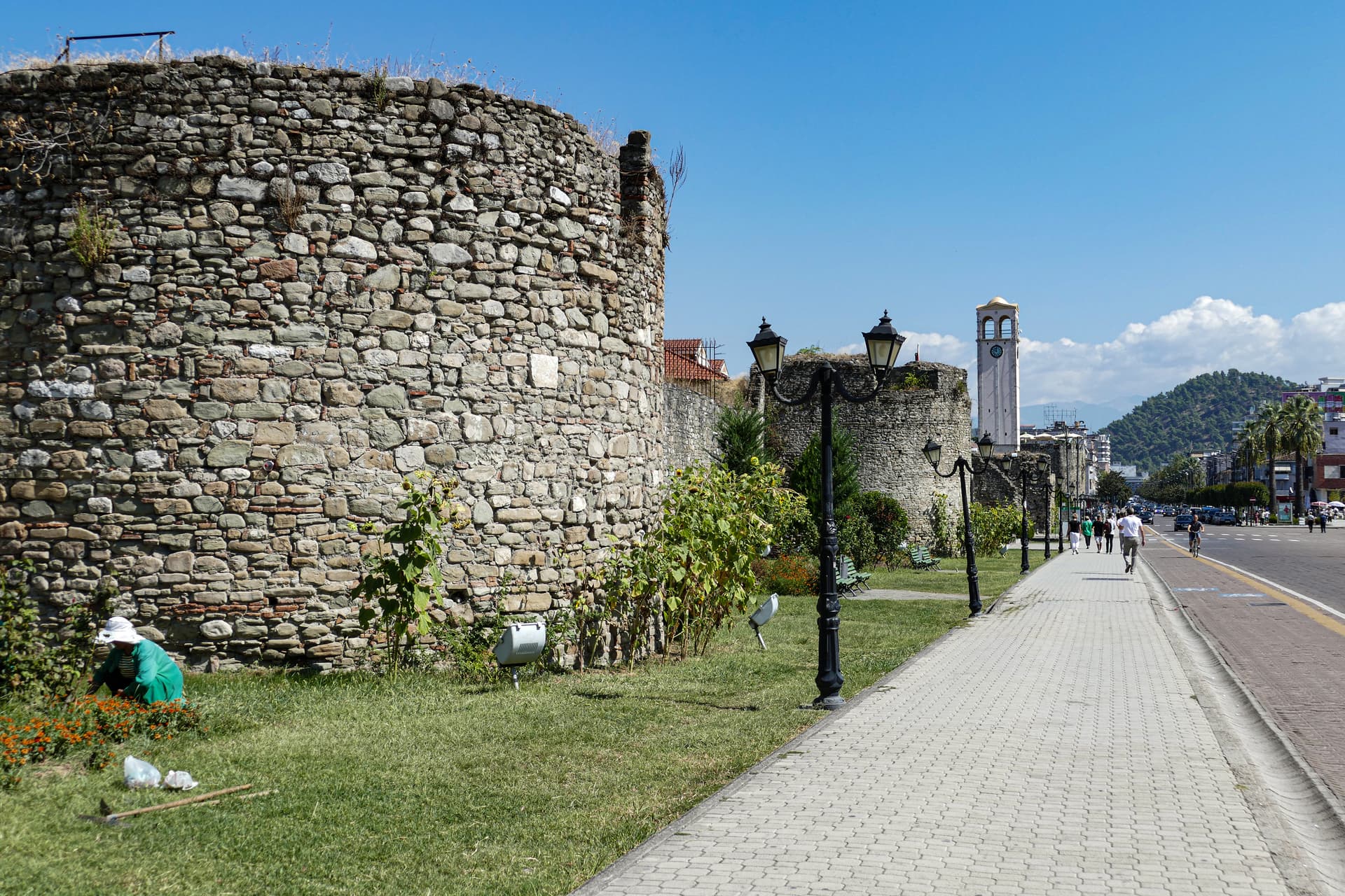 Stone castle walls and clock tower along a paved walkway in Elbasan, Albania.