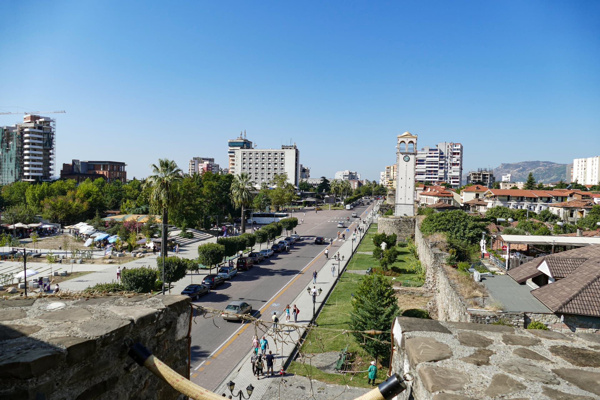 Clock tower overlooking a street, market stalls, and modern buildings in Elbasan, Albania.
