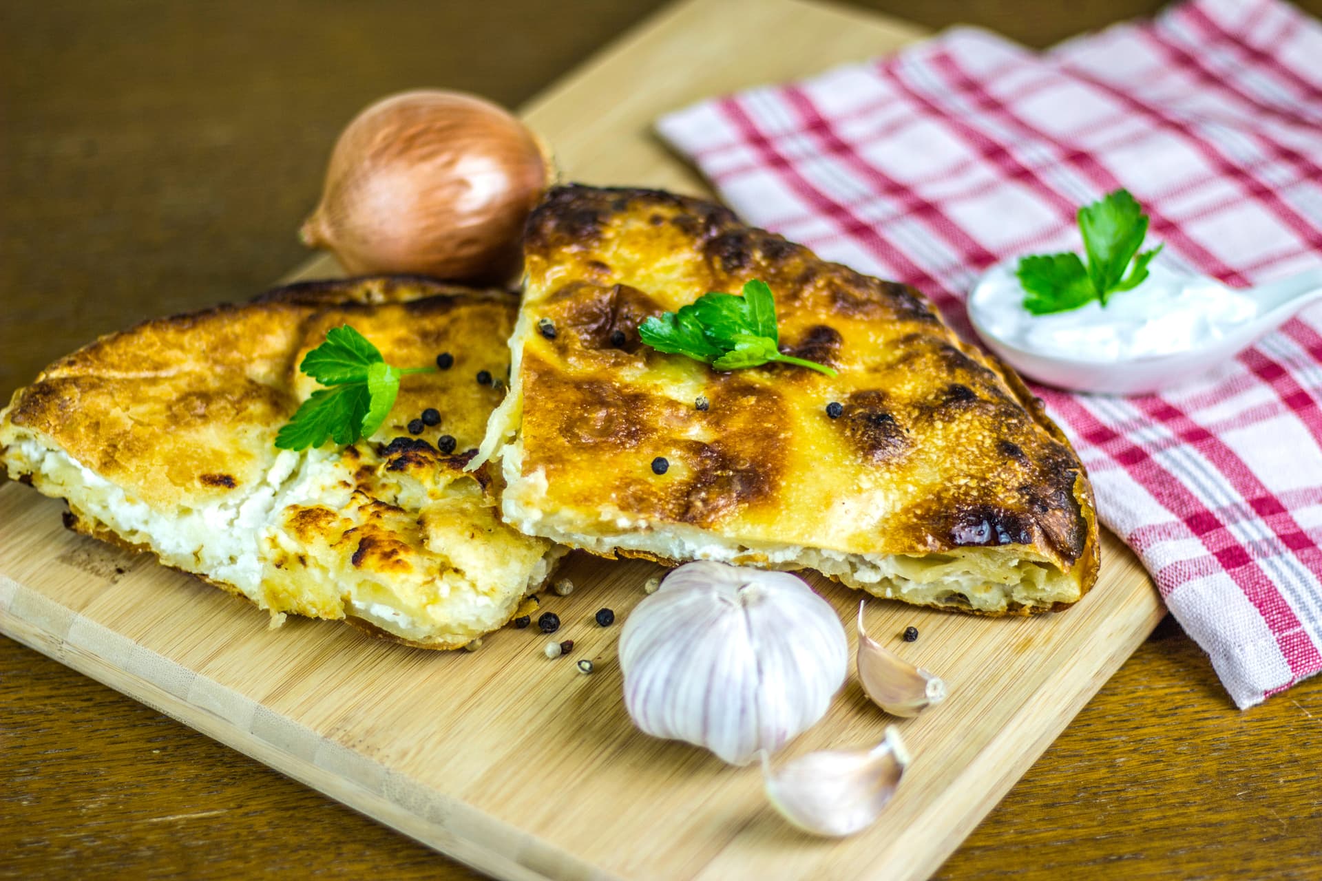 Five-cheese burek slices on a wooden board with onion, garlic, and yogurt dip, Albania.