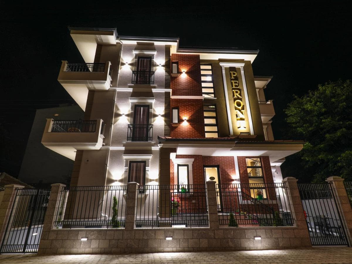 Illuminated Hotel Peroni building facade at night, secured by a black metal fence in Korce.