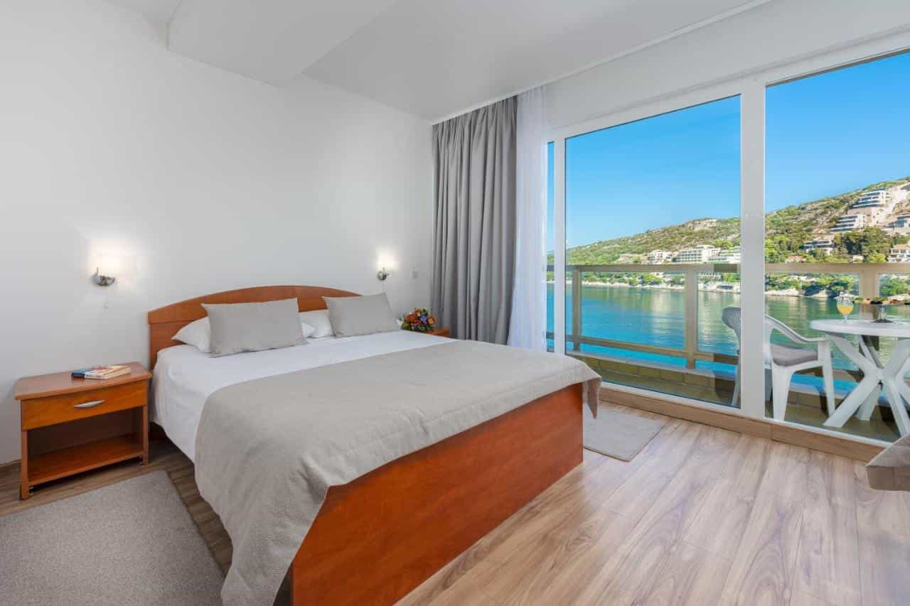 Hotel room with wooden bed and balcony overlooking the sea and green hills of Dubrovnik.