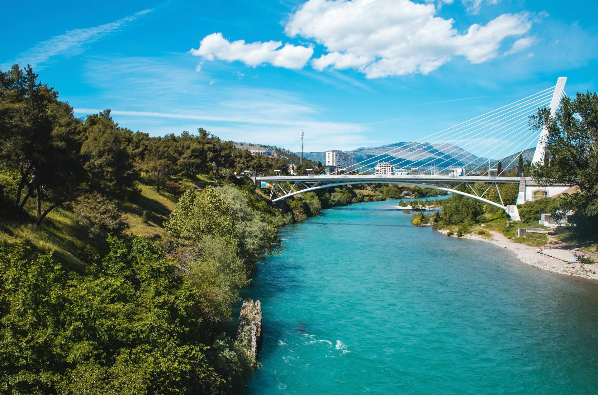 Cable-stayed bridge over turquoise Morača River with lush green banks in Podgorica, Montenegro.