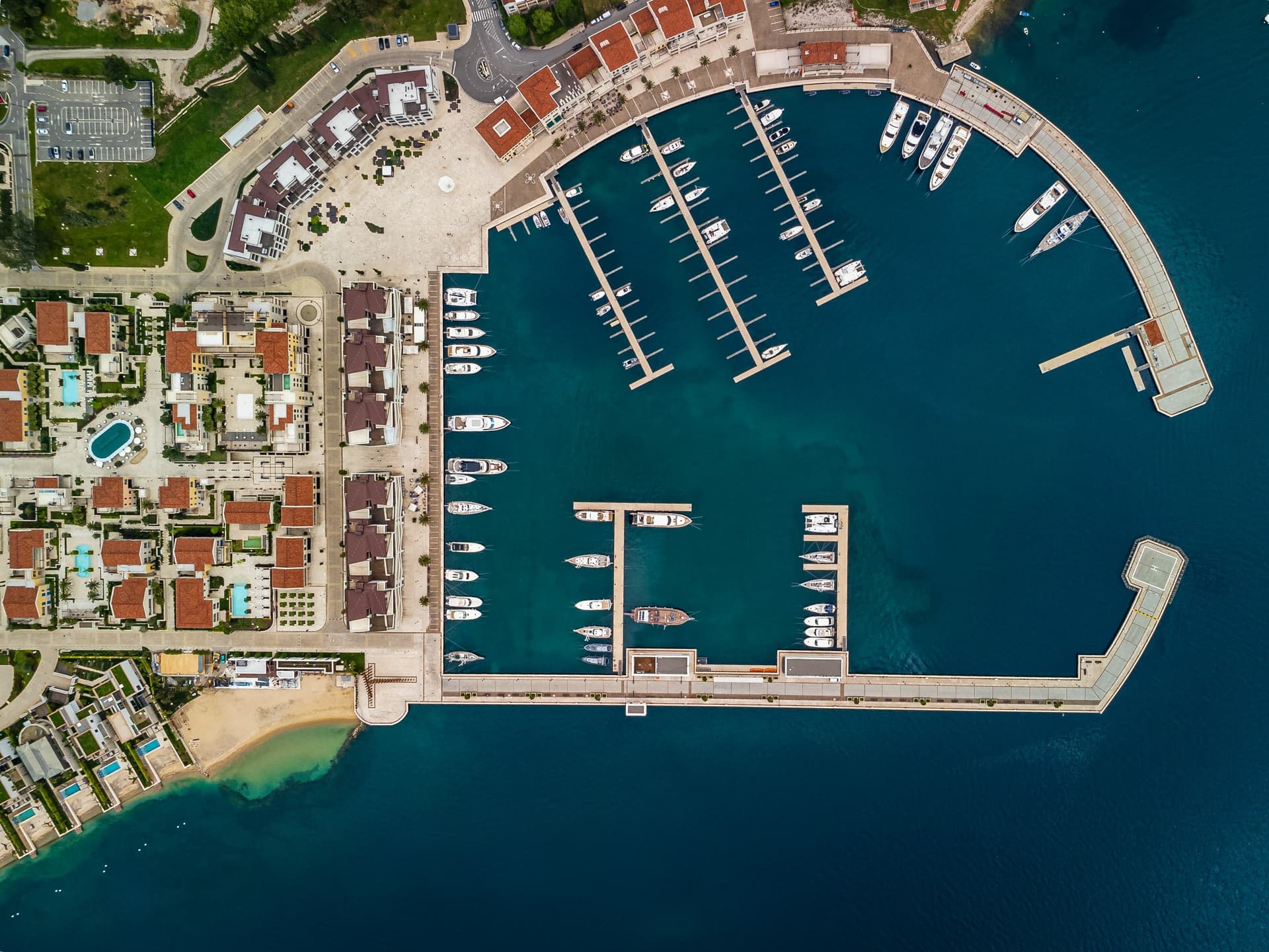 Aerial view of marina with docked boats, luxury residences, and swimming pools in Herceg Novi, Montenegro.