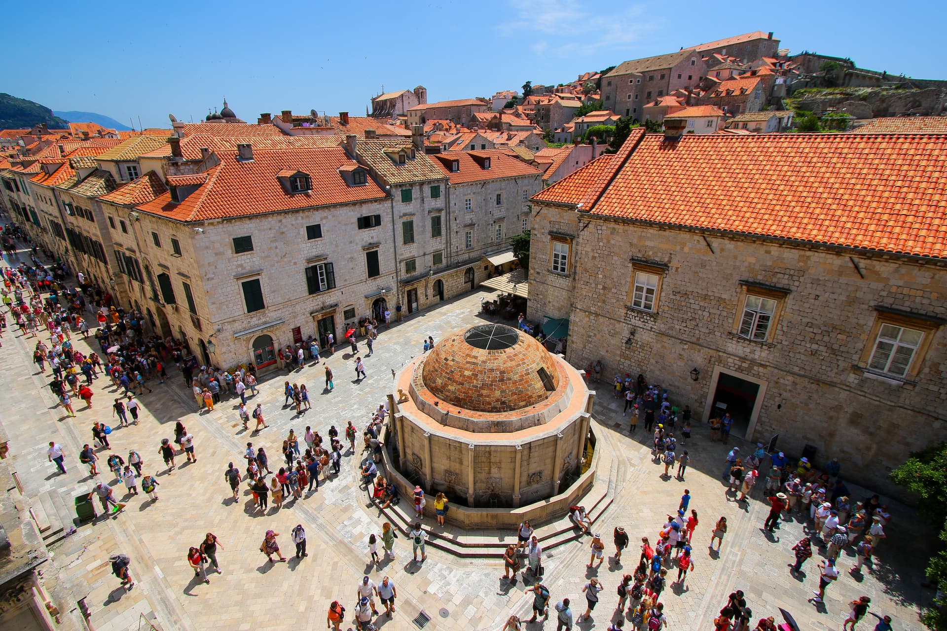 Onofrio's Fountain in a crowded stone square with historic buildings and red tile roofs in Dubrovnik, Croatia.