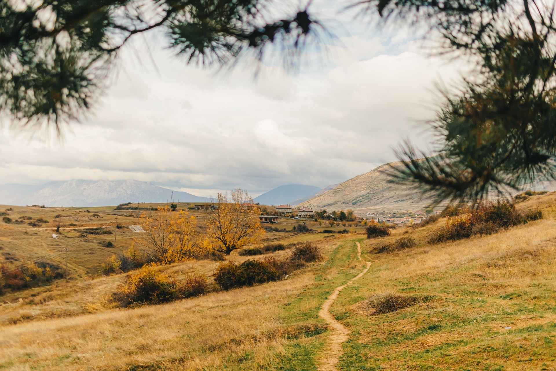 Winding dirt path through dry hills toward village and hazy mountains in Albanian hinterland.