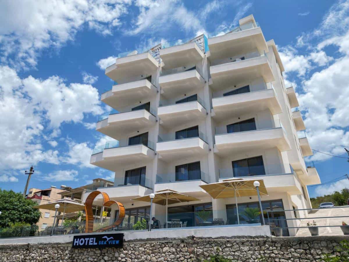 Modern white Sea View Hotel Saranda building with balconies under a bright blue, cloudy sky.