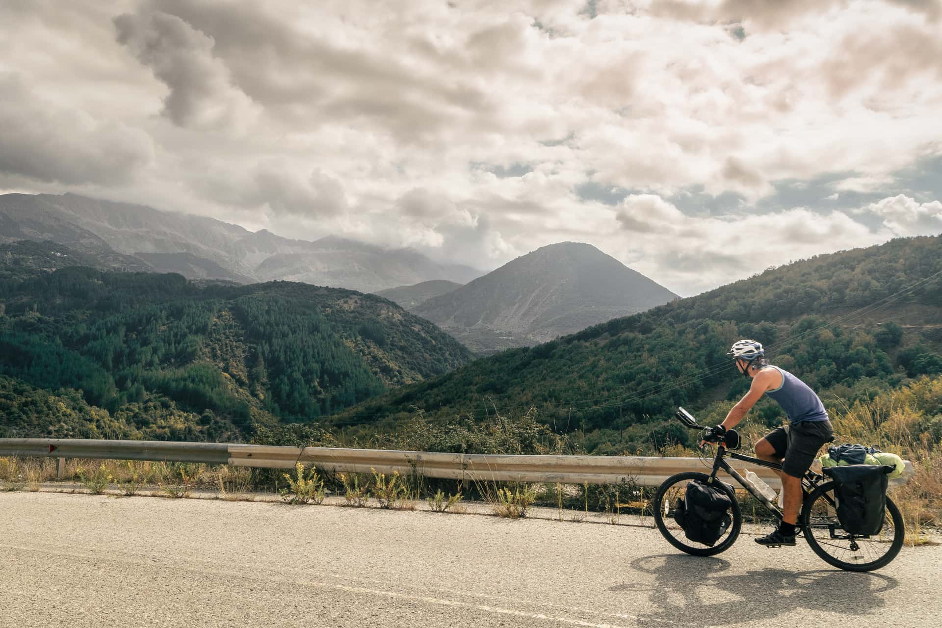 Cyclist bicycle touring on mountain road with scenic forested slopes and cloudy sky.